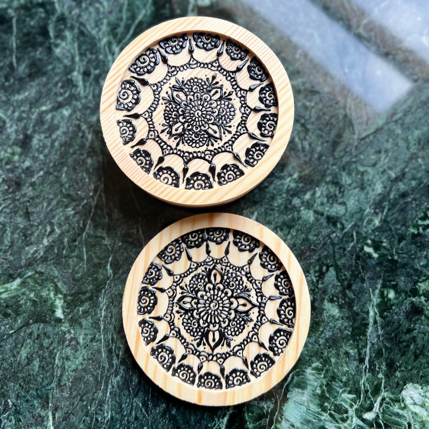 Close-up of detailed black henna-style mandala art on natural wooden coaster as a set of 2
