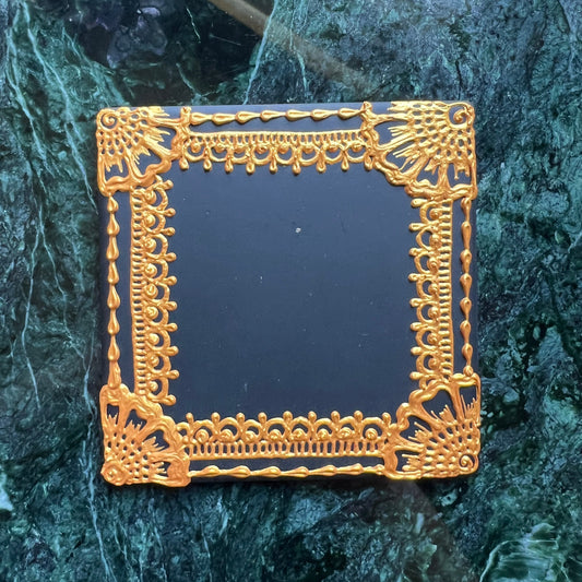 Top view of hand-painted ceramic coaster with gold henna border on black square tile