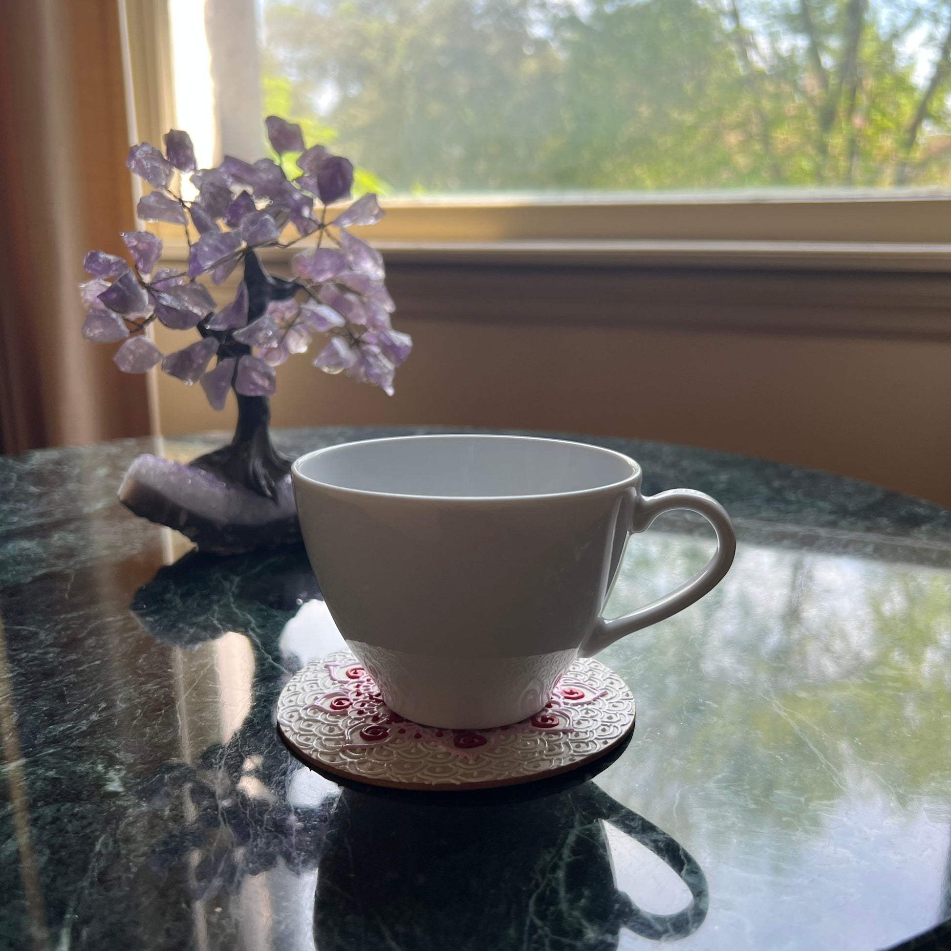 Red and pink floral mandala coaster styled for gifting or decor, ideal for handmade art lovers. Shown here in use with a cup on it. 