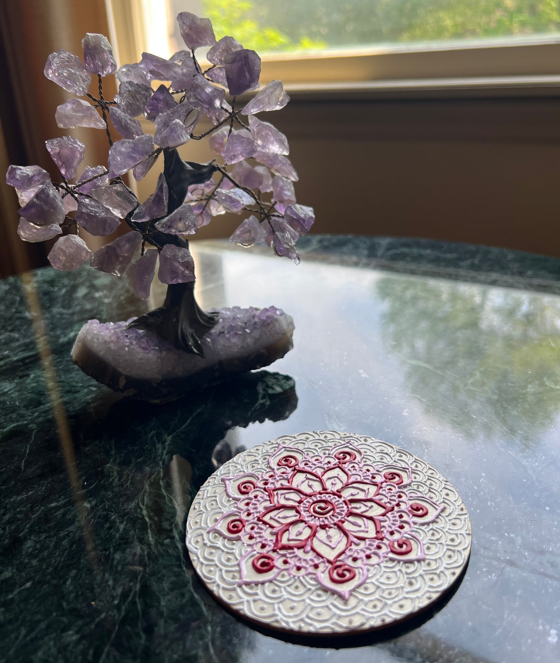 Side angle of hand-painted red and pink mandala wooden coaster showing raised details on natural wood