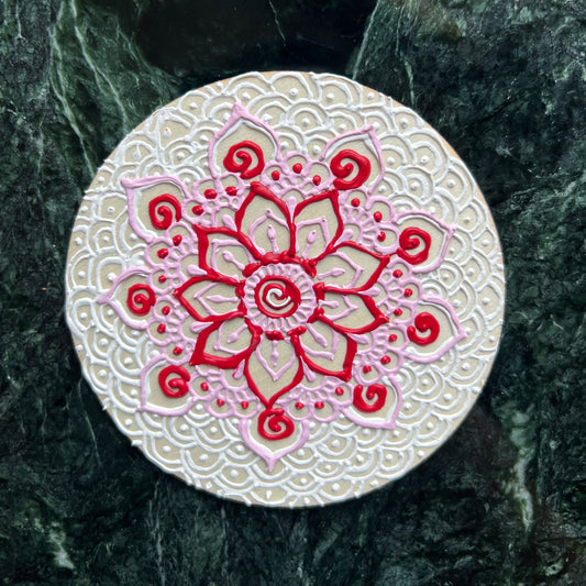 Hand-painted wooden coaster with red and pink floral mandala design, top view
