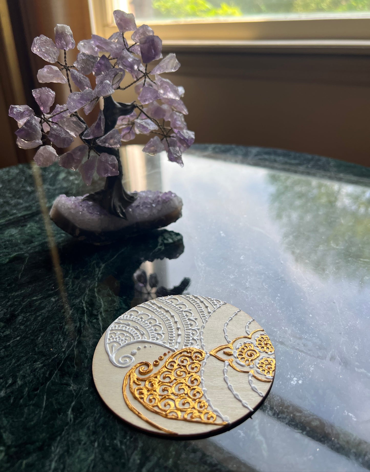 Side angle of hand-painted wooden coaster with white and gold paisley henna design showing raised paint texture on natural wood
