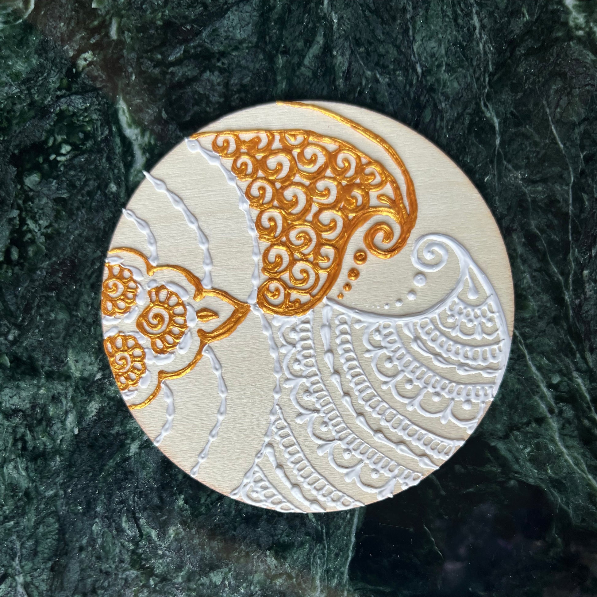 Top view of hand-painted wooden coaster with white and gold paisley henna design
