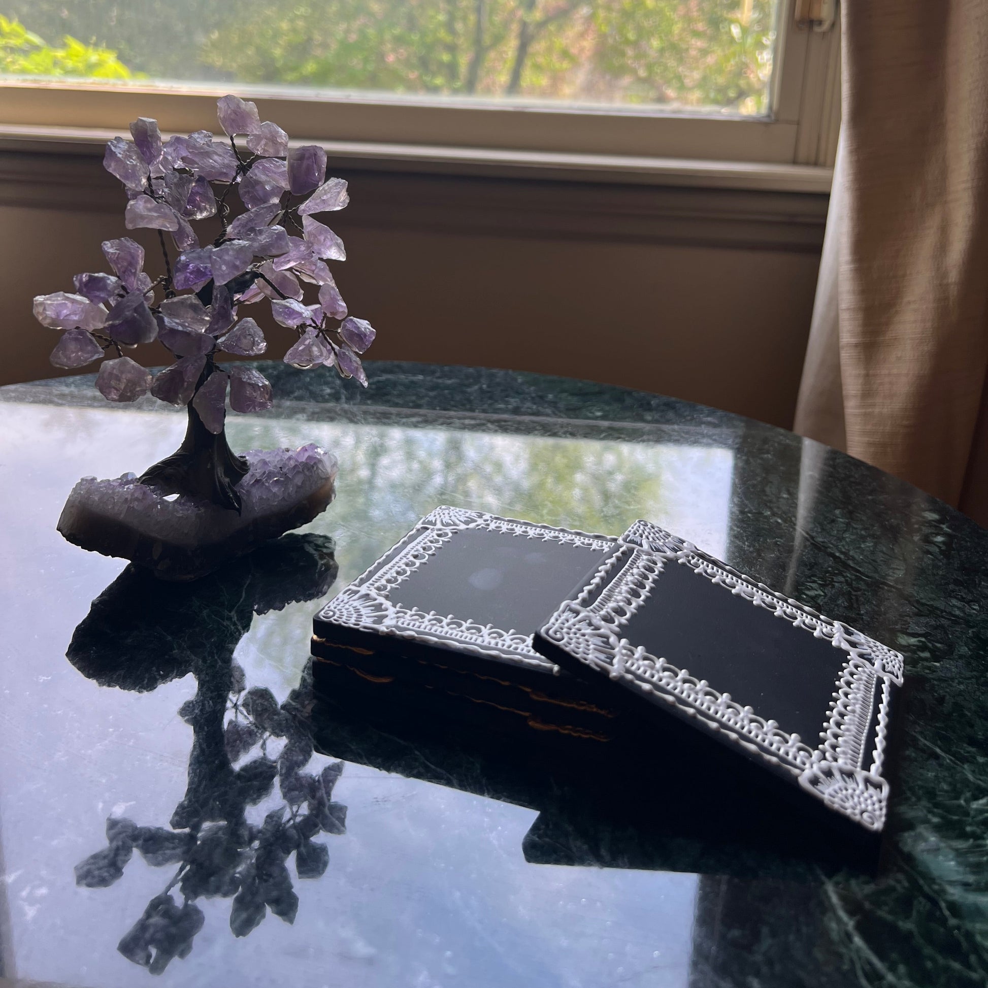 Side view of hand-painted black ceramic coaster with intricate white henna border design, square tile format